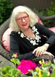 Photo of instructor Josie Emmons Turner sitting in a patio chair with statement-red glasses frames and a big smile.